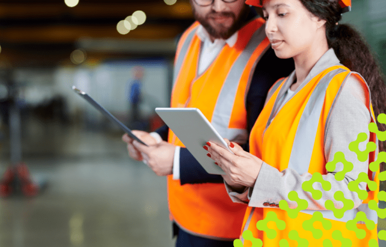 Factory workers in safety vests and hard hats looking at tablets.