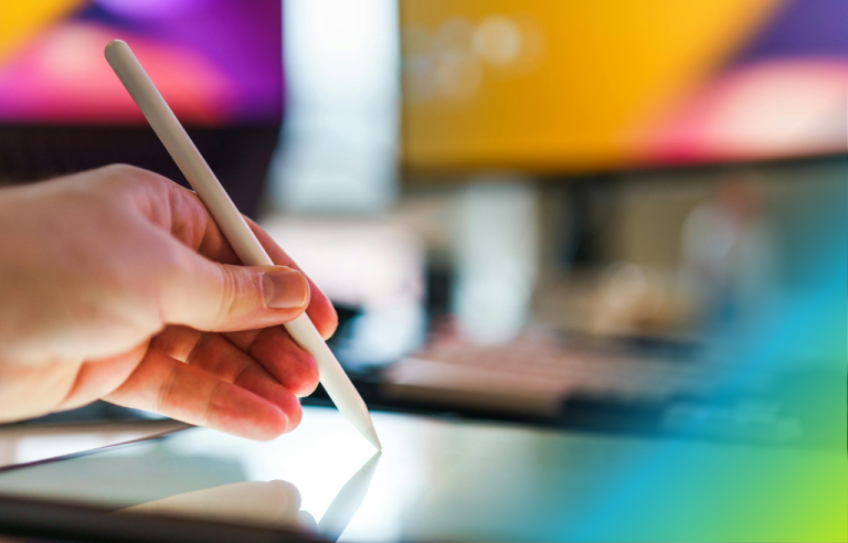 close up of hand holding a stylus pressed on top of a tablet with colorful background.