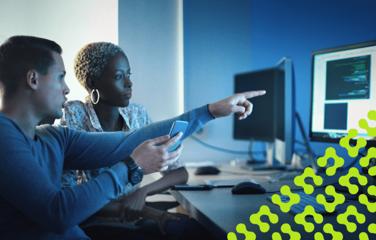 A woman and man working late at night in an office, intently focused on multiple computer screens.
