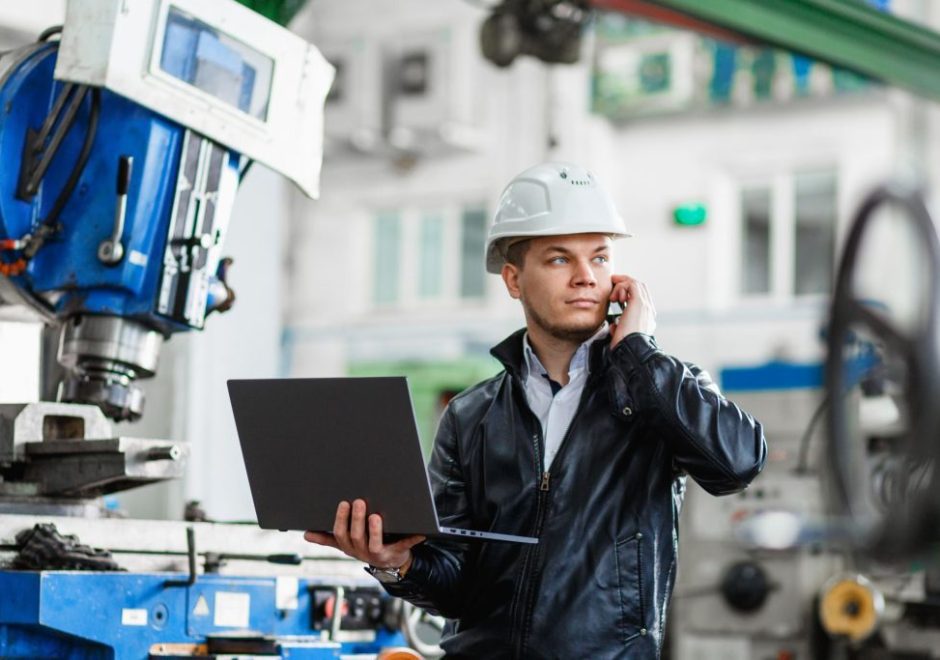 Leverage your data to drive decisions man wearing a helmet while taking a phone call and using a laptop at a manufacturing plant