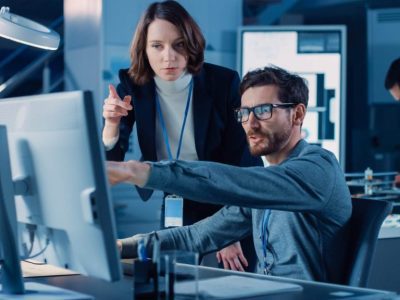 Are you at the crossroads of choosing between staying the course with SAP ECC 6, migrating to the next generation of SAP Business Suite S/4HANA Man and woman discussing solutions in front of a computer in business environment
